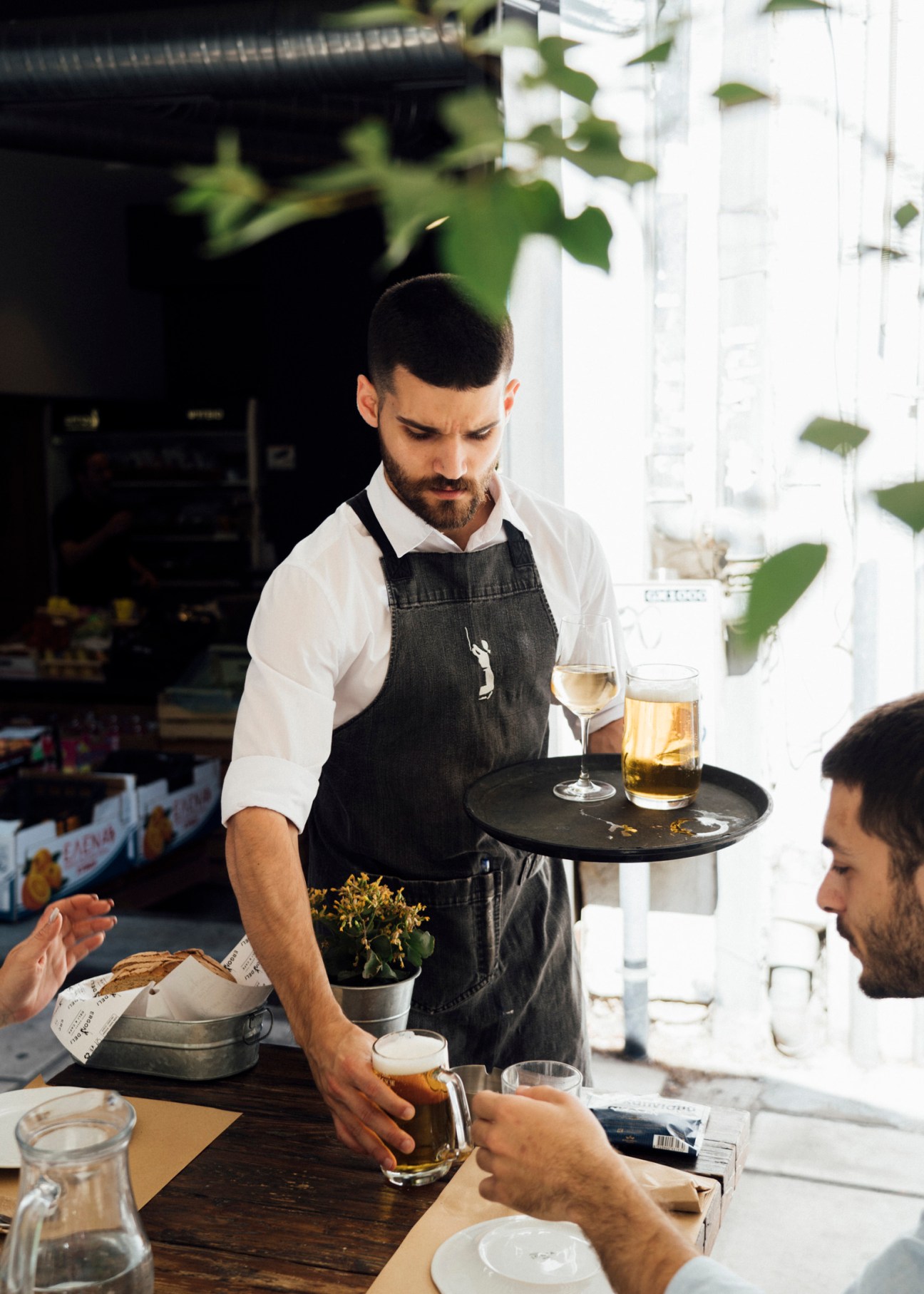 Bartender serves drinks at a bright café with ivy-covered walls in Thessaloniki.