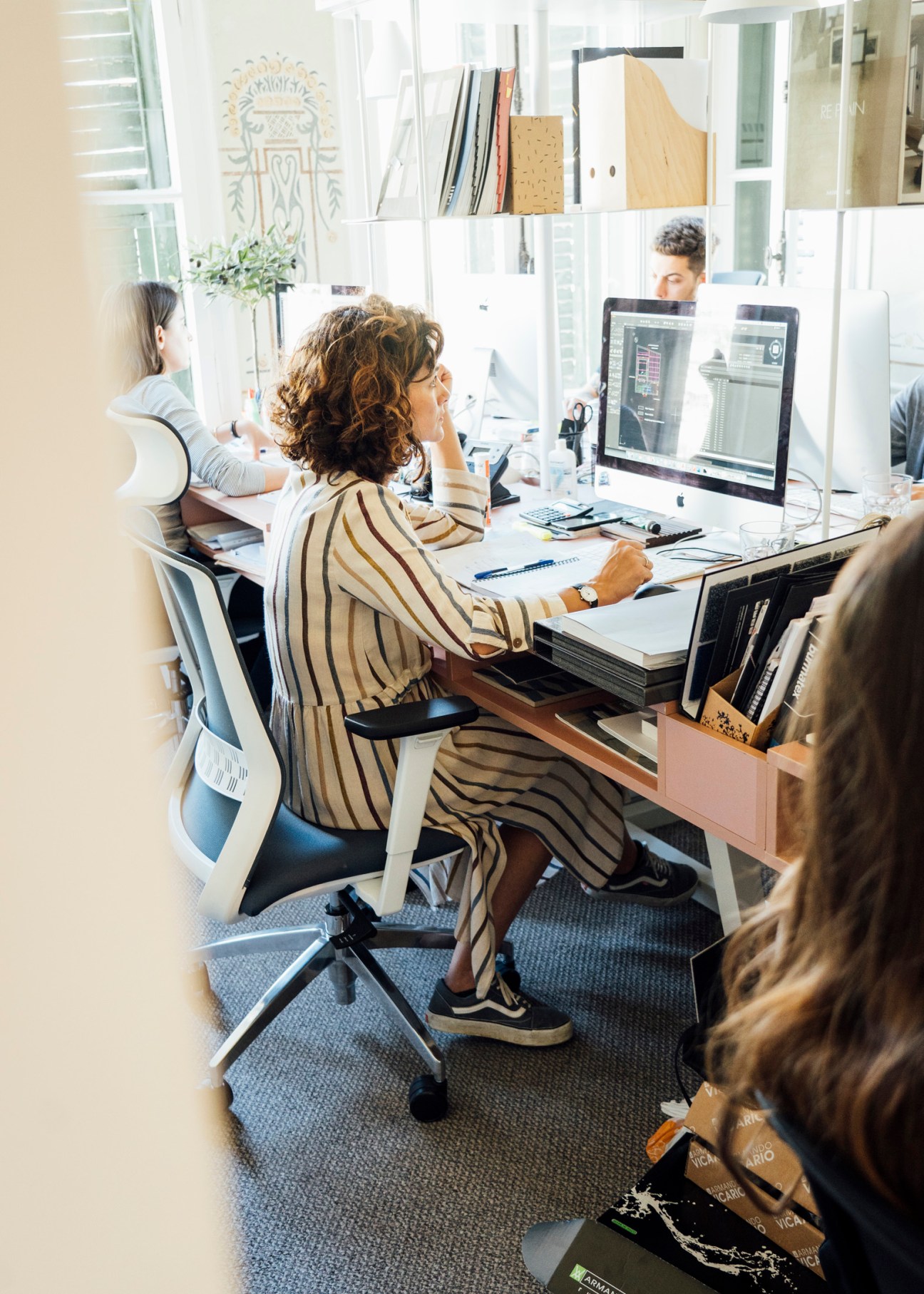 Woman at desk working on computer in modern office with white shelving and natural light