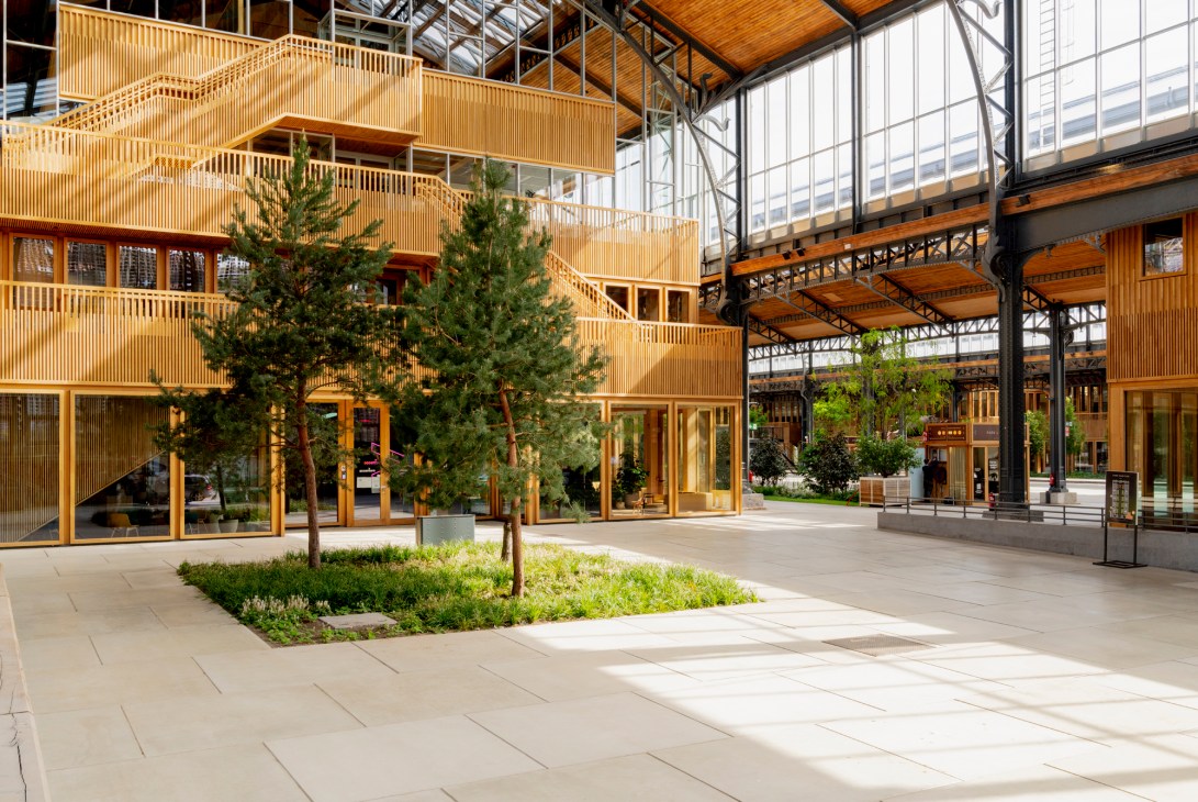 Interior courtyard of the Gare Maritime with wooden architecture, glass ceiling, greenery and modern retail spaces.