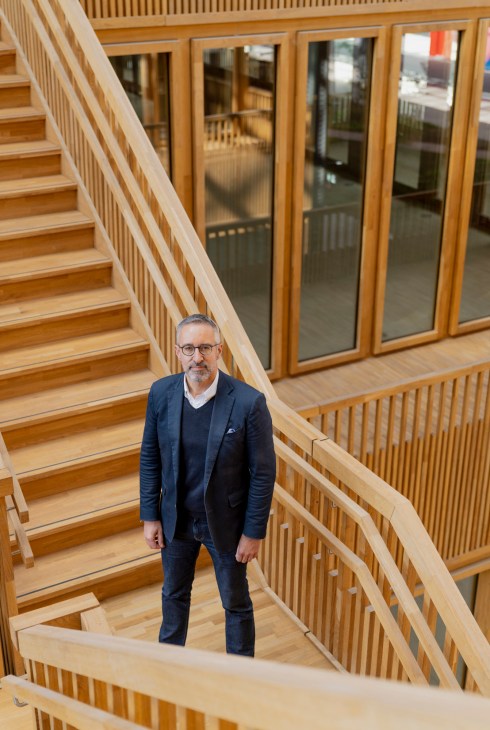Kris Verhellen, CEO of Extensa, stands on a wooden staircase in a modern interior with large windows and wooden railings.