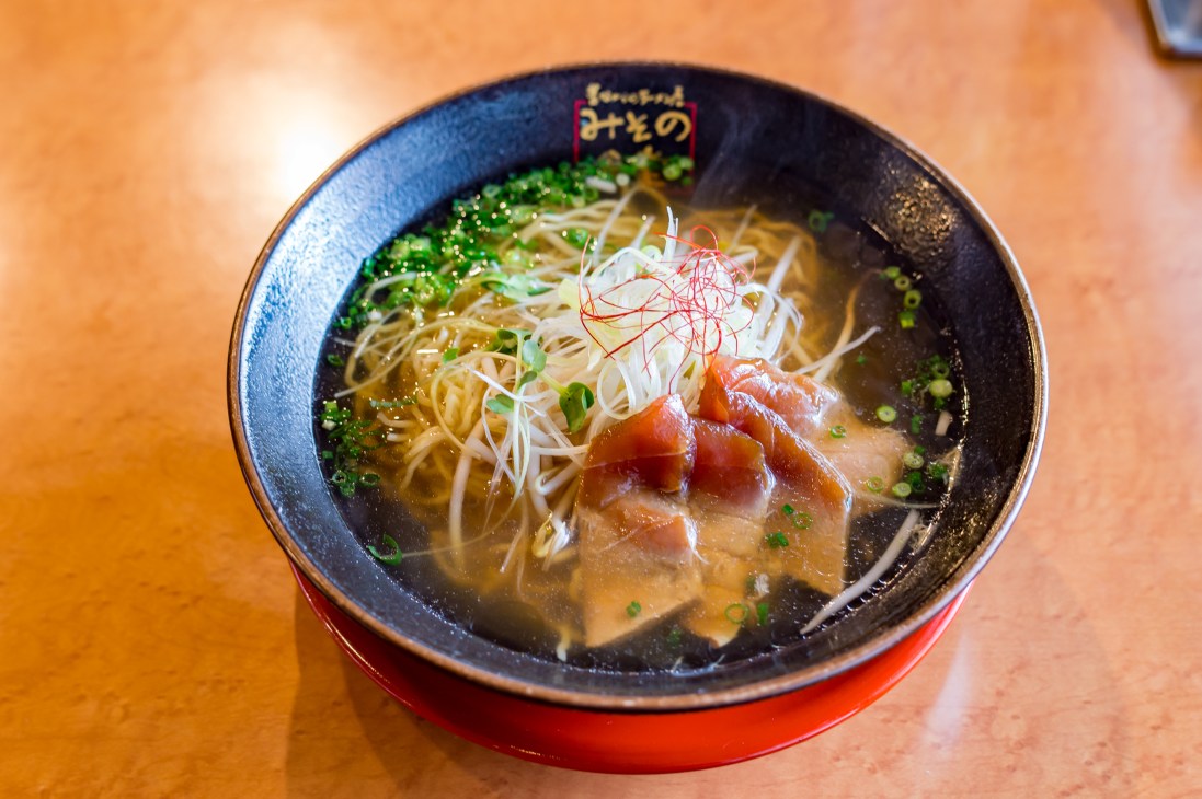 Bowl of tuna ramen with noodles, sliced fish, bean sprouts and garnish in dark bowl