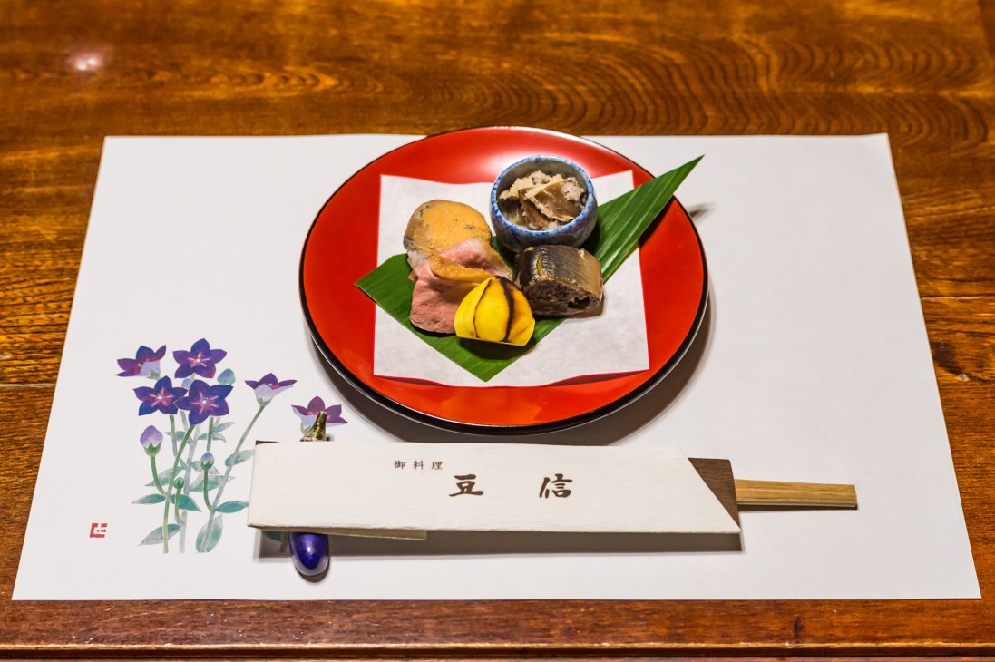 Japanese kaiseki dinner served on a red lacquered plate with fish, vegetables and garnishes at Mameshin restaurant.