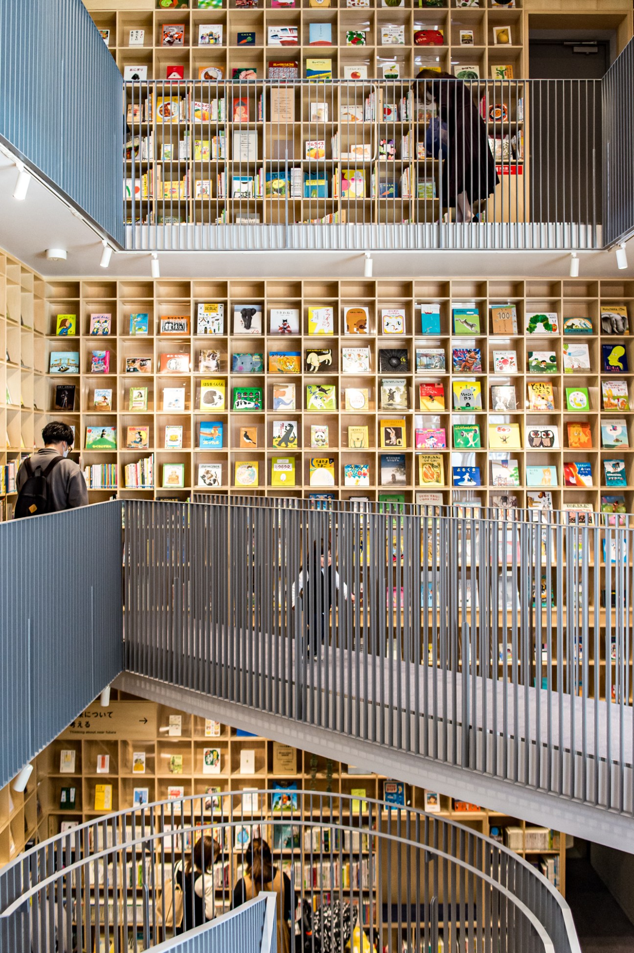 Multi-level library interior with floor-to-ceiling wooden bookshelves and metal railings spanning three stories