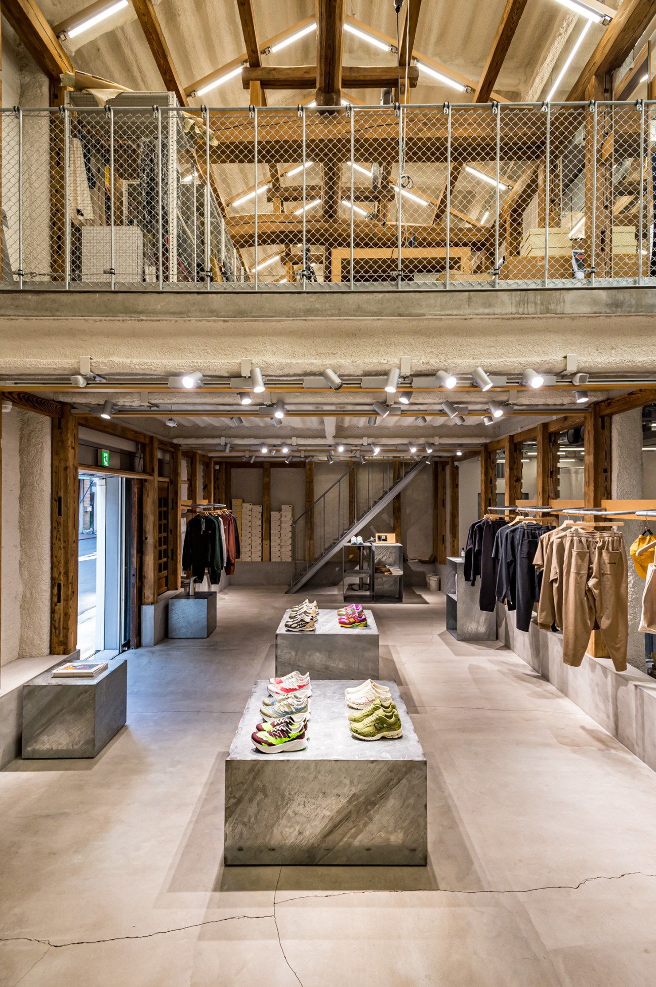 Modern retail interior with exposed wooden beams, concrete displays, clothing racks, and sneakers on pedestals