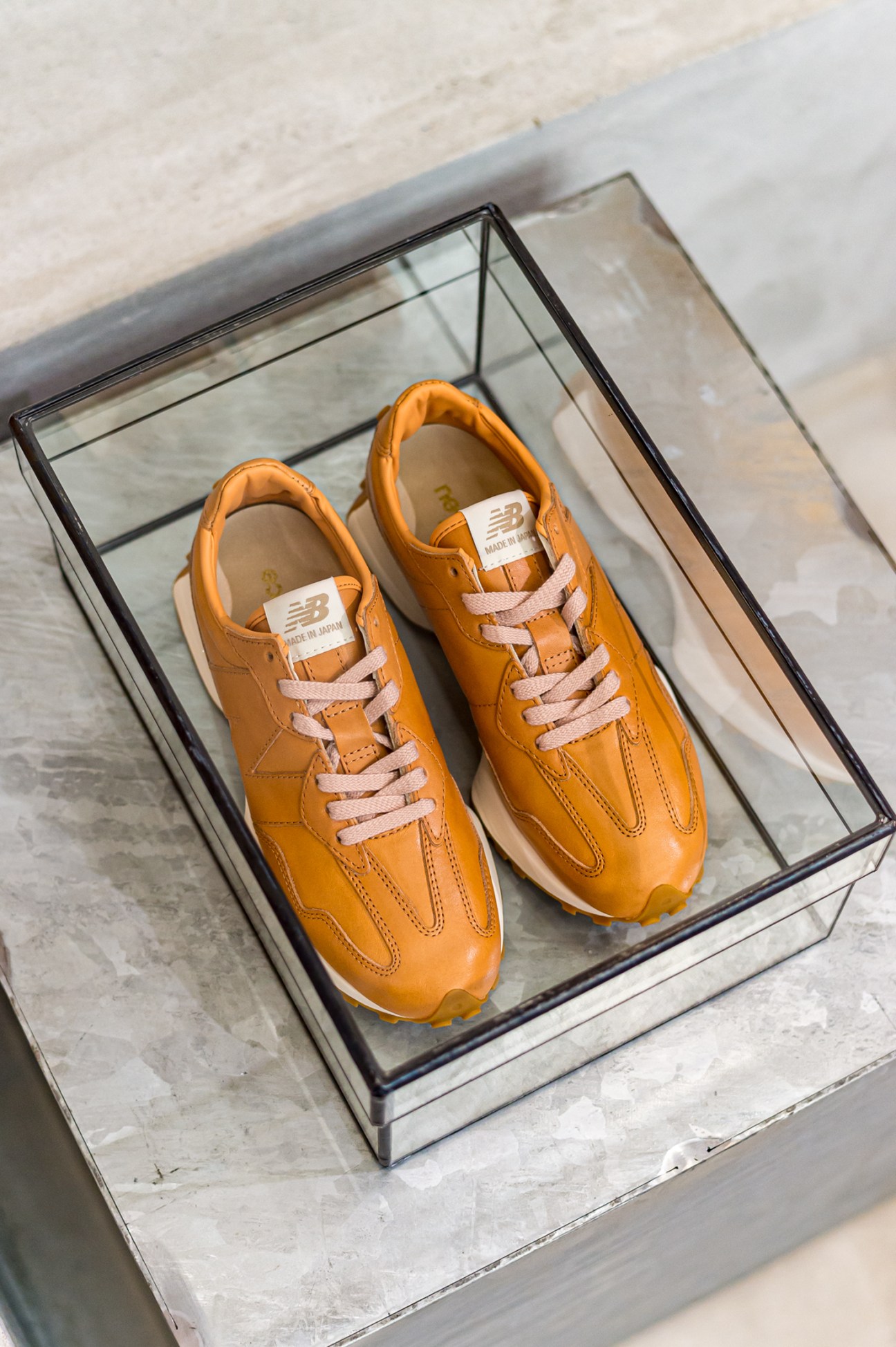 Orange New Balance trainers displayed in a clear acrylic display box