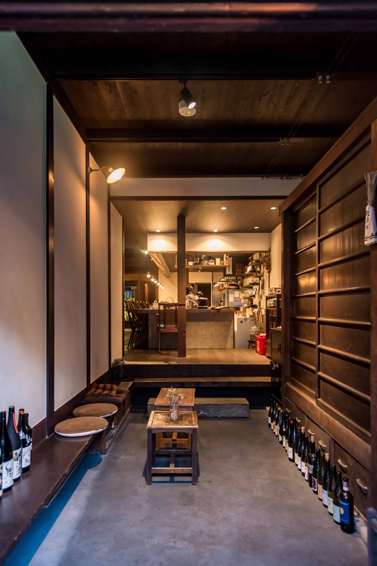 Traditional Japanese restaurant interior with low seating, wooden shelves lined with sake bottles, and open kitchen