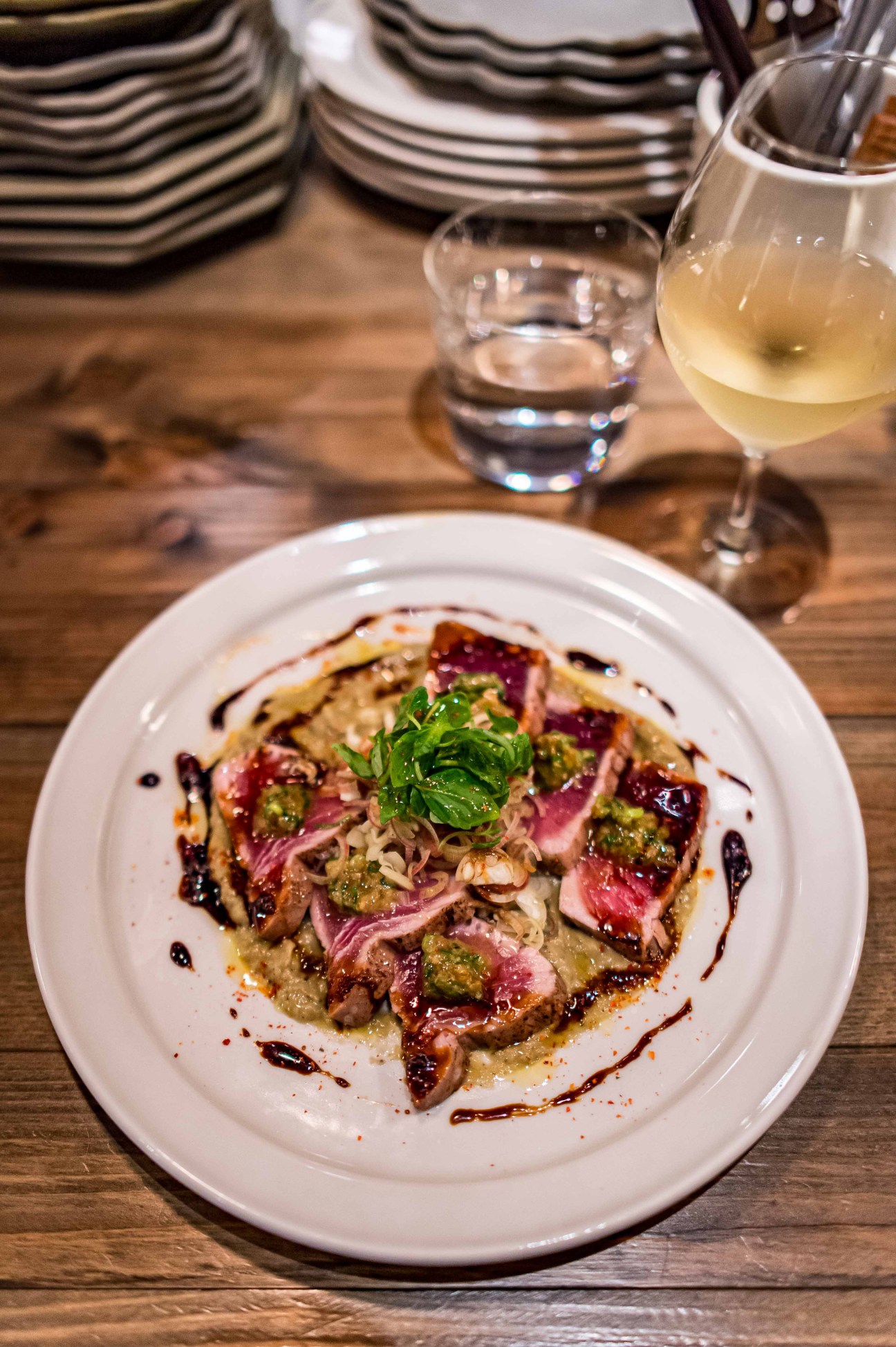 Seared tuna dish with aubergine purée, garnished with herbs and drizzled with dark sauce, served with white wine