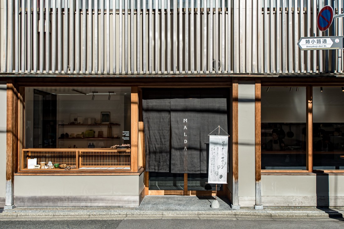 Malda hotel storefront in Kyoto with white vertical slats, wooden framing, and traditional noren curtain entrance.