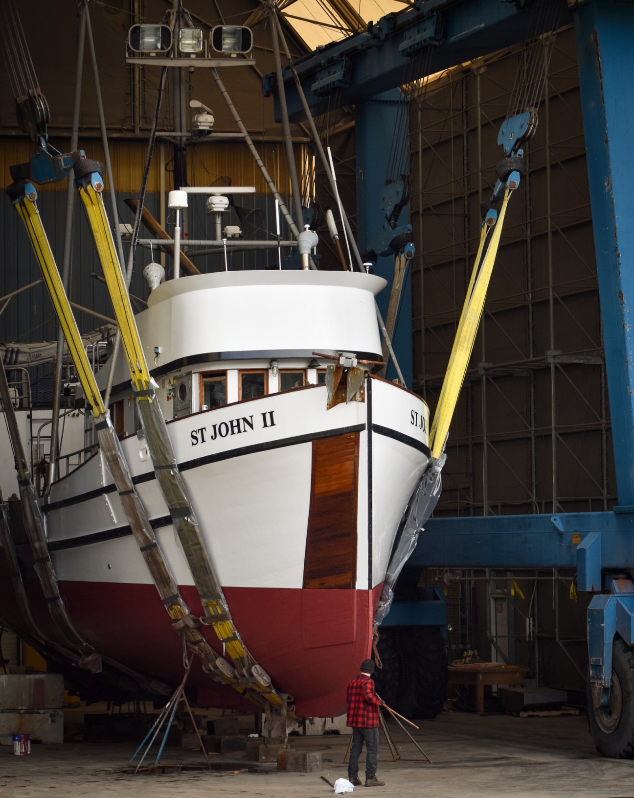 Boat named St John II suspended by yellow straps in Port Townsend Shipwrights Co-Op repair facility
