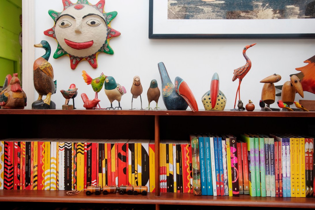 Colorful decorative bird figurines and folk art displayed on wooden bookshelf above books