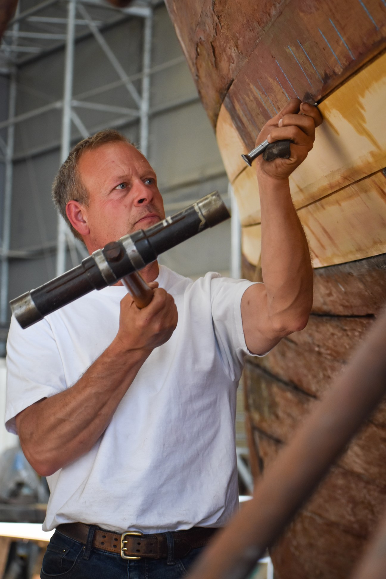 Craftsman using hand tools to work on wooden boat restoration at shipwright workshop