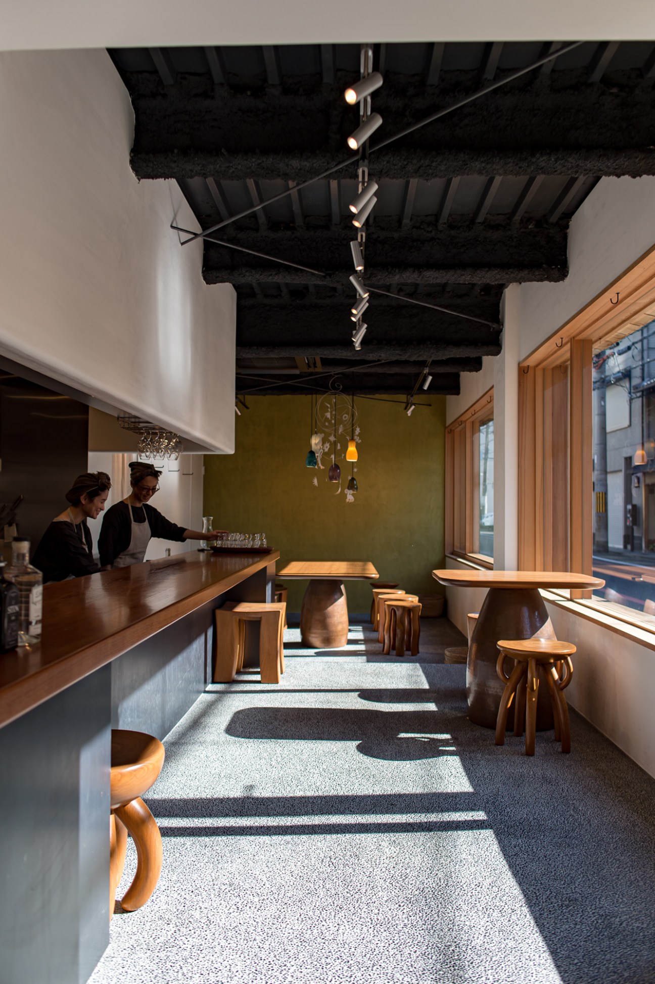 Café Malda interior with wooden counter, staff member, olive green wall, and wooden furniture.