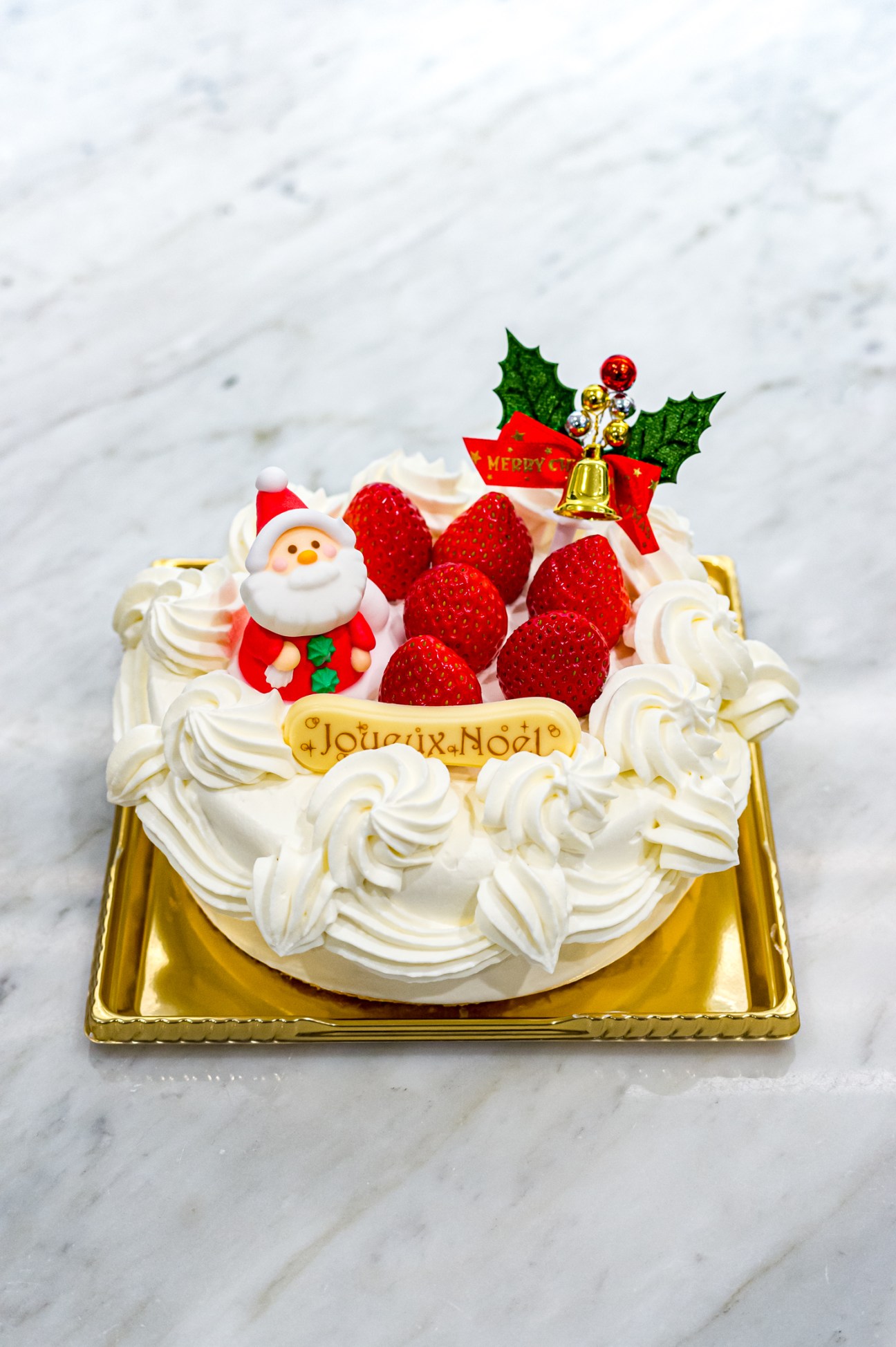 Japanese Christmas strawberry shortcake decorated with whipped cream piped swirls, fresh red strawberries, and Santa topper on gold base.