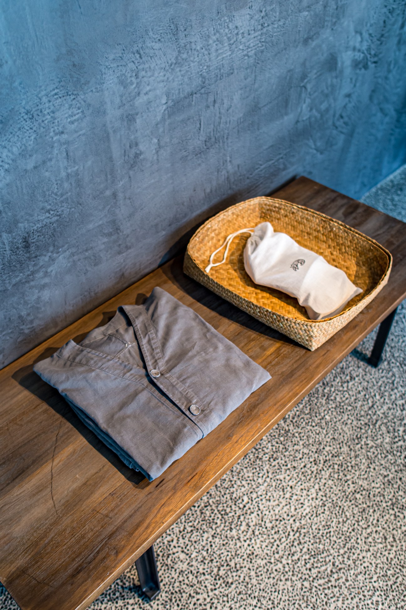 Folded organic cotton loungewear and white socks displayed in a woven basket on a wooden table at Malda Kyoto.
