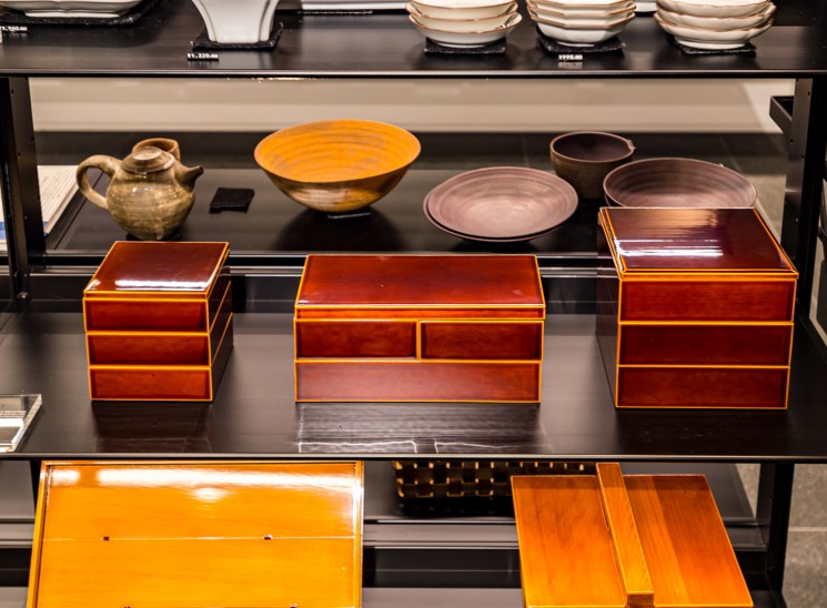Display shelves showing white ceramic bowls and plates on upper levels, with brown lacquered wooden boxes below
