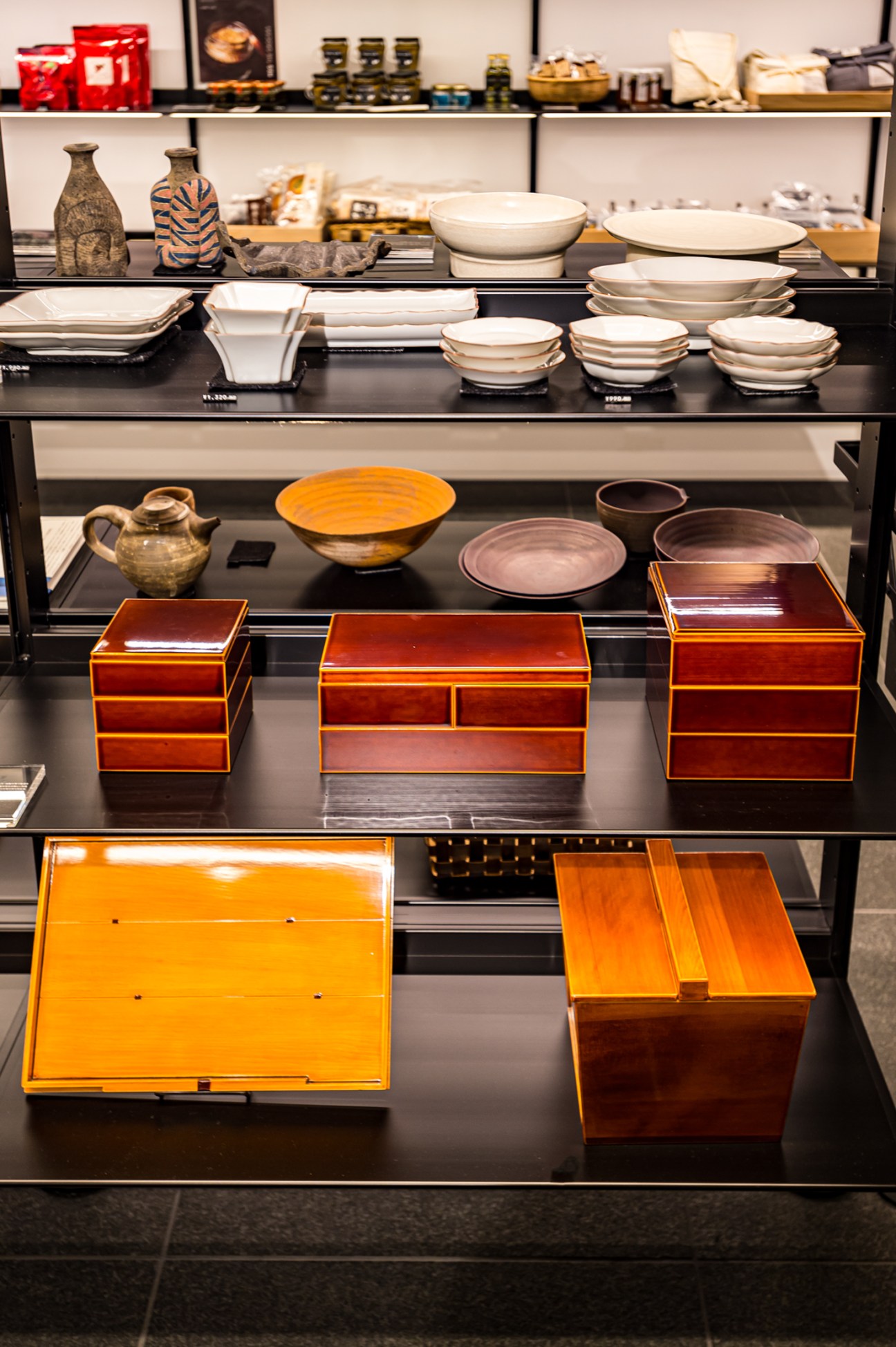 Display shelves showing white ceramic bowls and plates on upper levels, with brown lacquered wooden boxes below