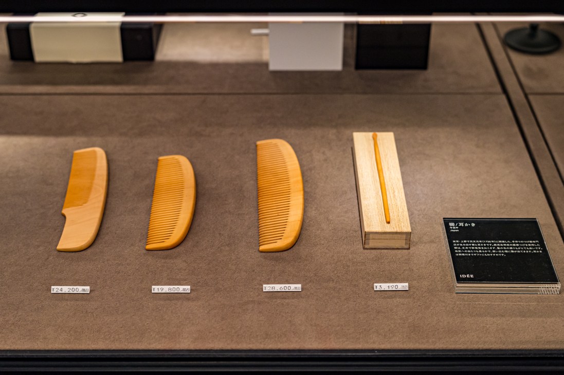 Four wooden combs and a wooden comb case displayed in a museum showcase with price labels