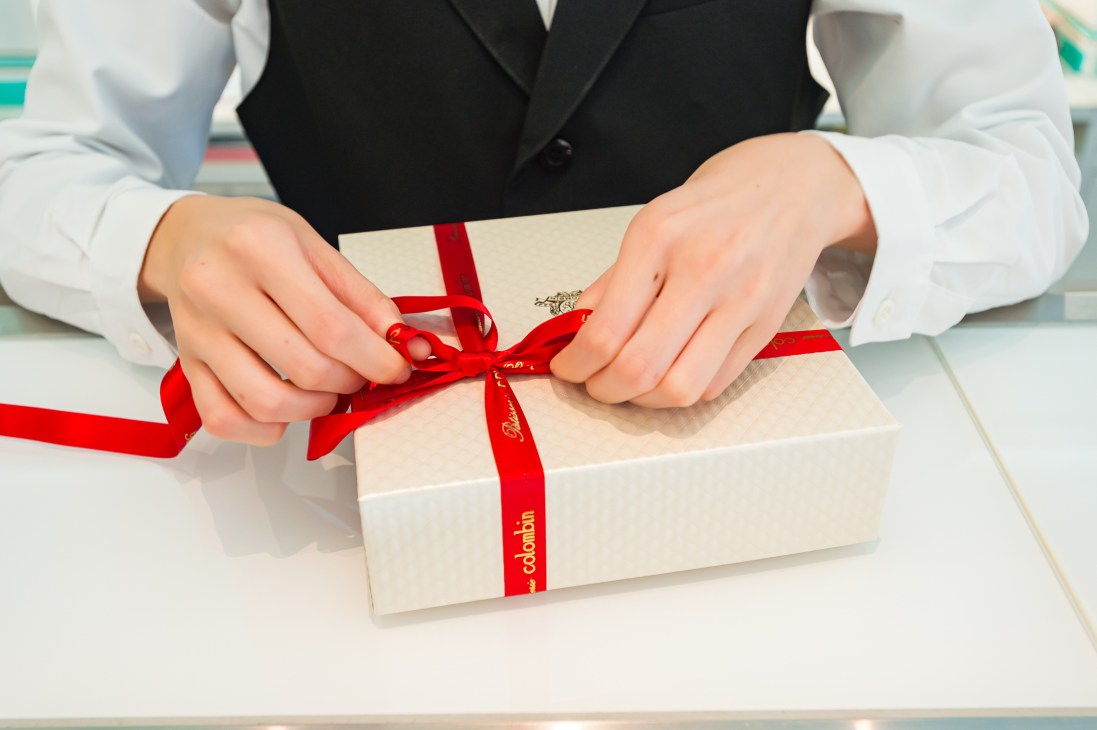 Hands tying a red ribbon bow on a cream-colored Colombin branded box.