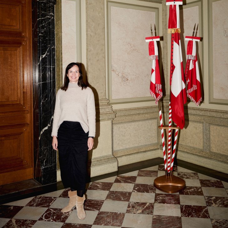Pälvi Pulli standing in an ornate government building interior with checkered marble floor and Swiss flags