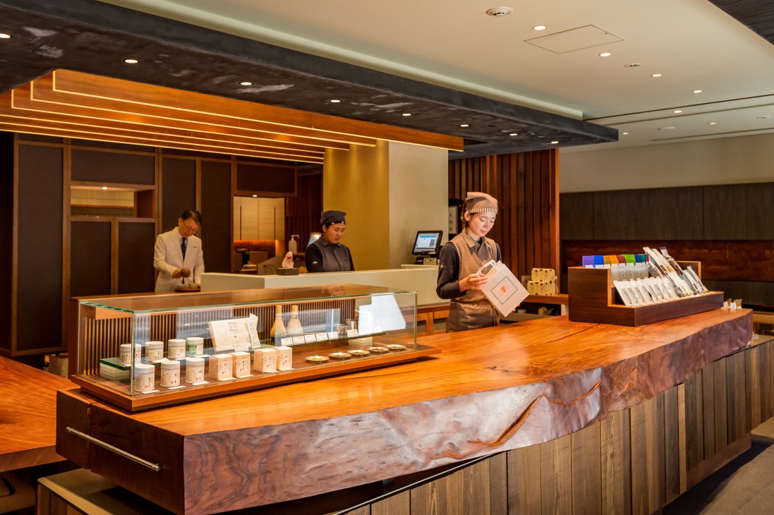 Interior of Ippodo tea shop with staff behind wooden counter displaying tea products and color-coded tea samples