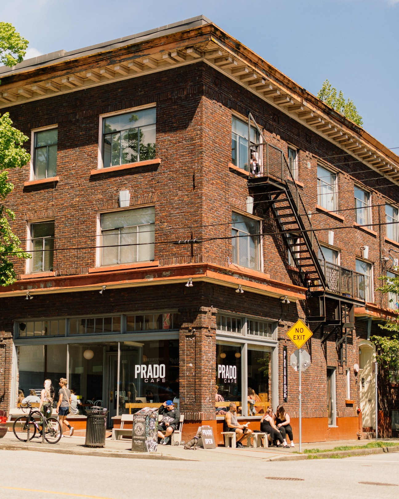Modern brick building with PRADO CAFE signage and outdoor seating area with people dining