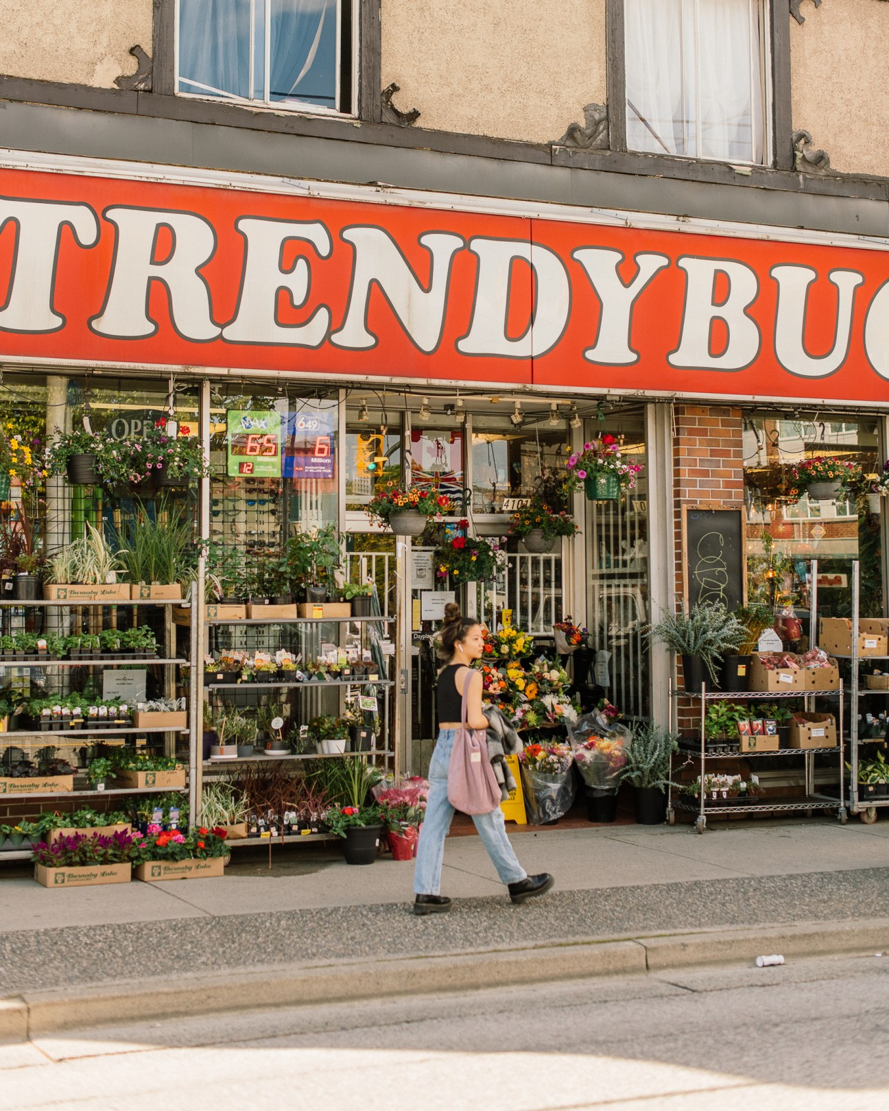 Woman walking past a flower shop with colorful blooms displayed outside the storefront