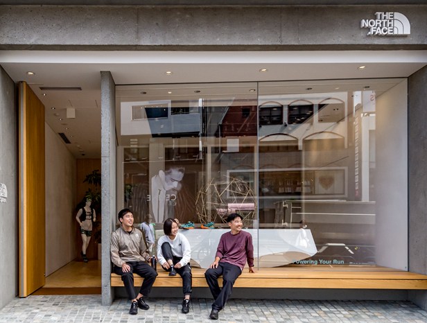 Three people sitting on wooden bench outside The North Face store window display