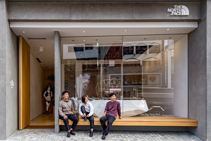 Three people sit on a wooden bench outside The North Face Sphere storefront in Tokyo.
