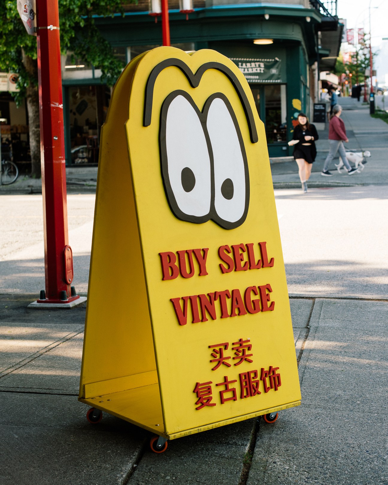 Yellow cylindrical advertising sign with cartoon eyes reading 'BUY SELL VINTAGE' in English and Chinese characters