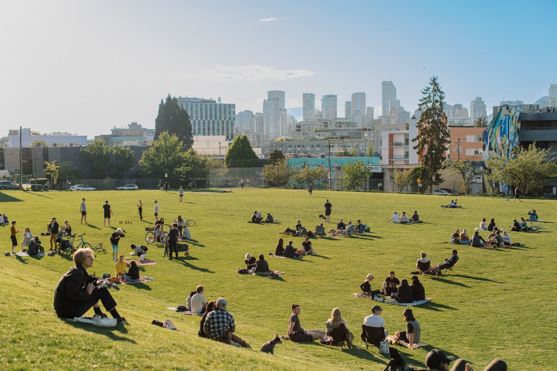 People relaxing on green grass in an urban park with city skyline in background
