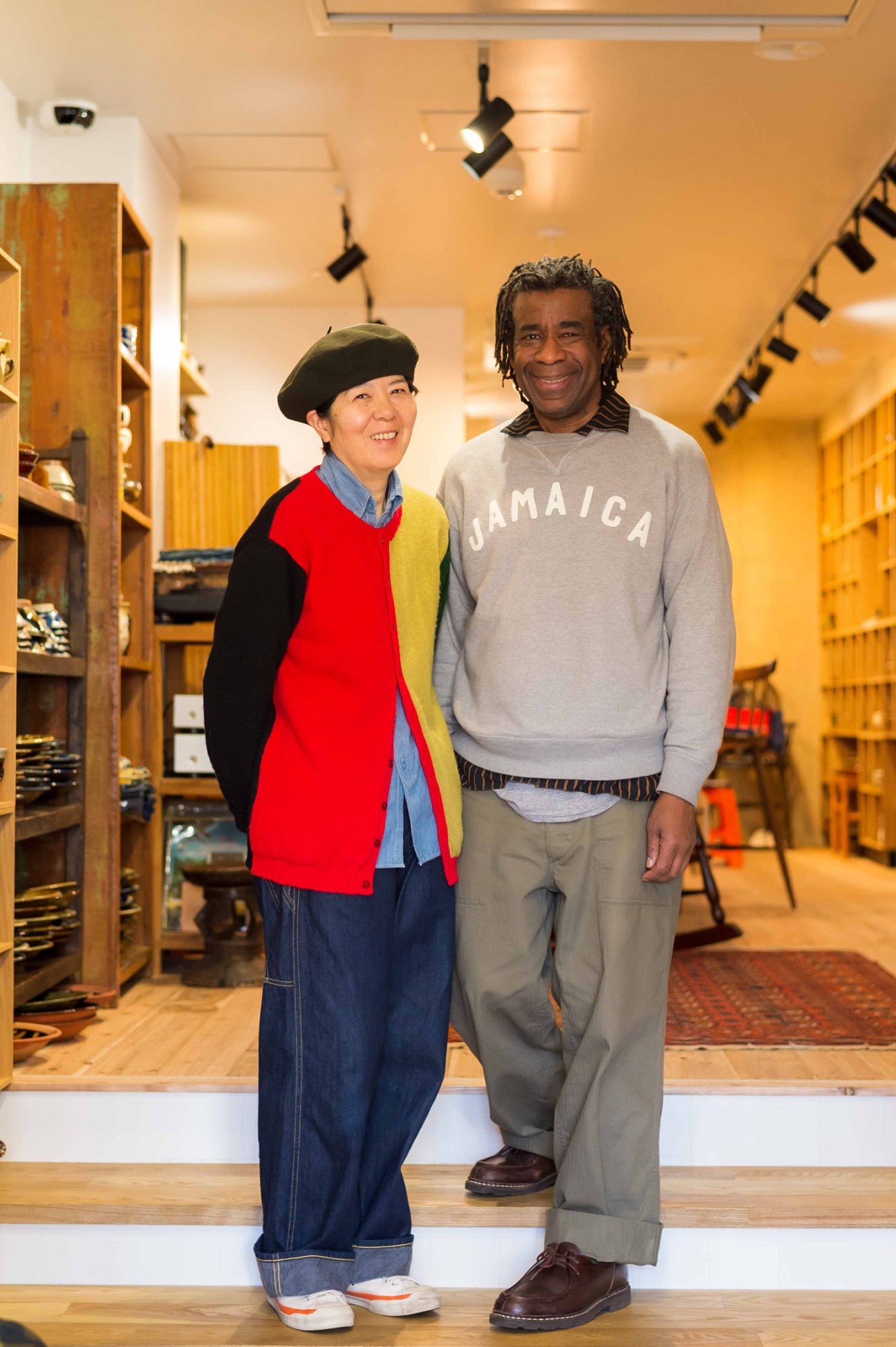 Two people standing in a retail shop interior with wooden shelving and track lighting.