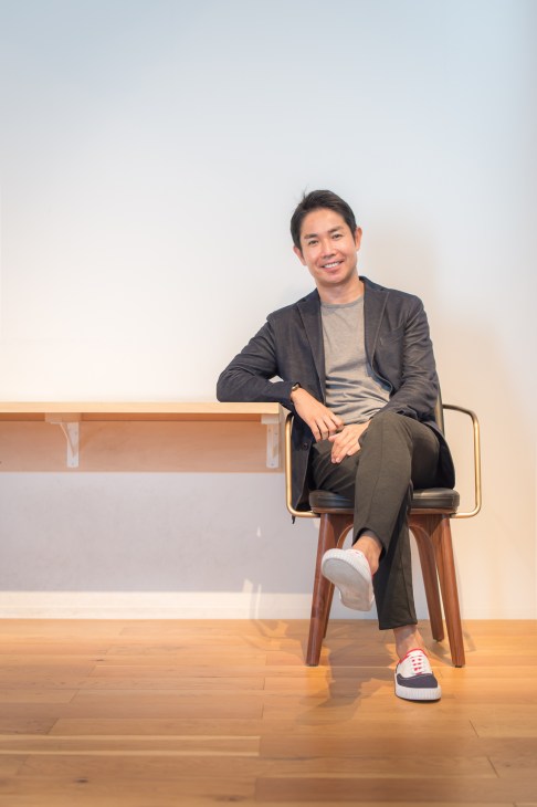 Yuichiro Hori, CEO of Stellar Works, sitting on a mid-century modern chair in a minimalist showroom.