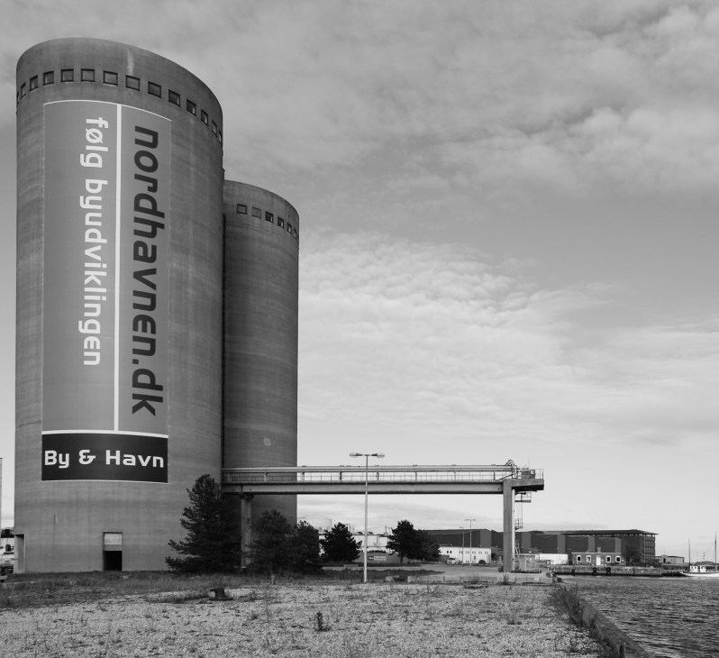 Two cylindrical concrete industrial silos with text signage reading nordhaven.dk and By & Havn along Copenhagen's waterfront