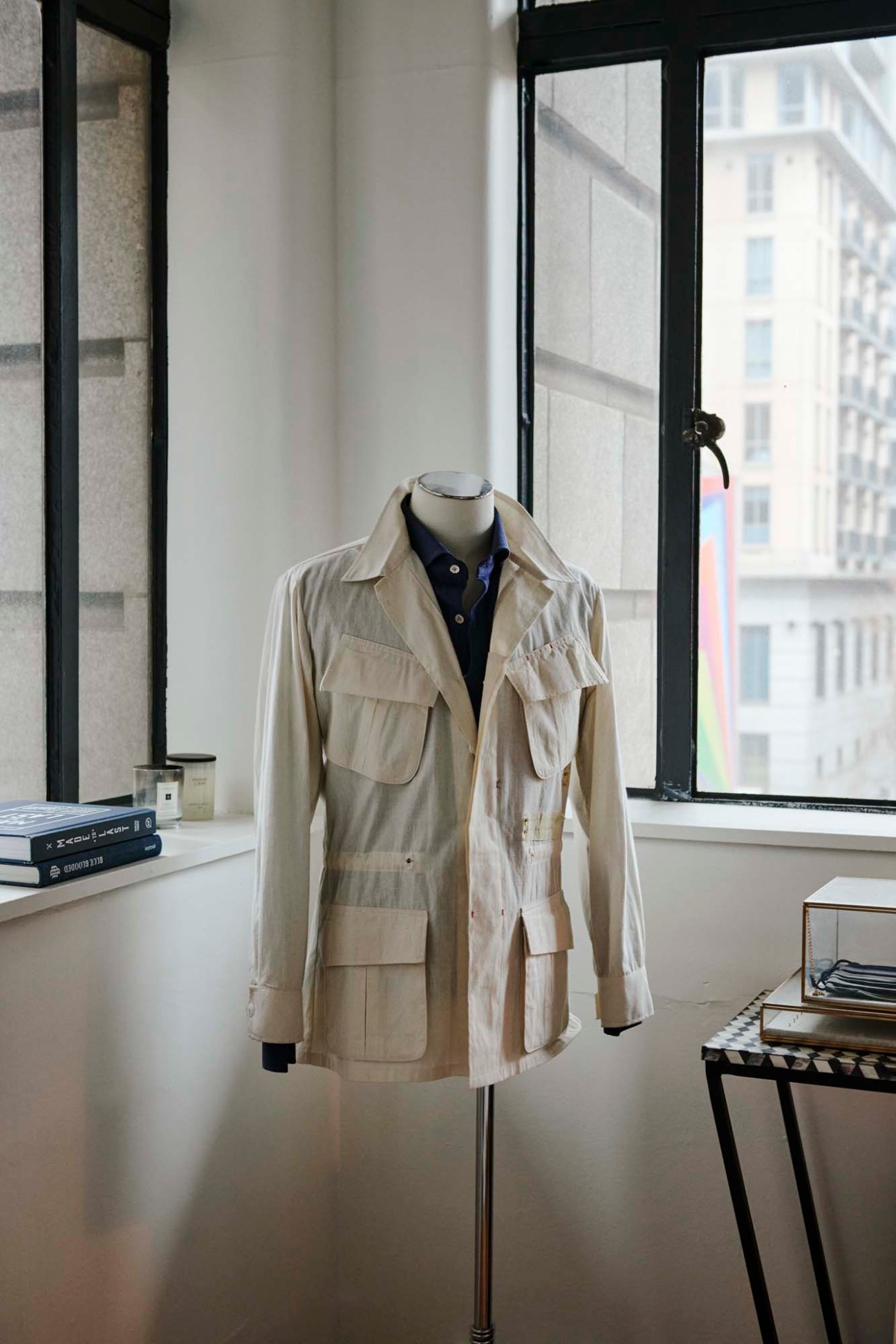 Beige safari-style overshirt with multiple chest pockets displayed on a mannequin in a bright window-lit interior.