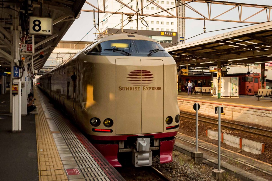 Sunrise Express sleeper train at platform 8 showing beige and red exterior with Japanese station infrastructure