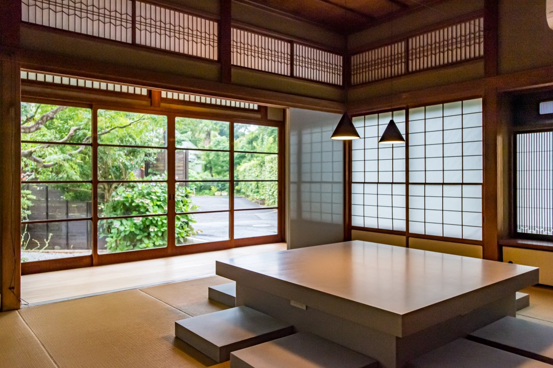 Tatami-floored meeting room with low table, pendant lights, and shoji-screened windows overlooking a garden.