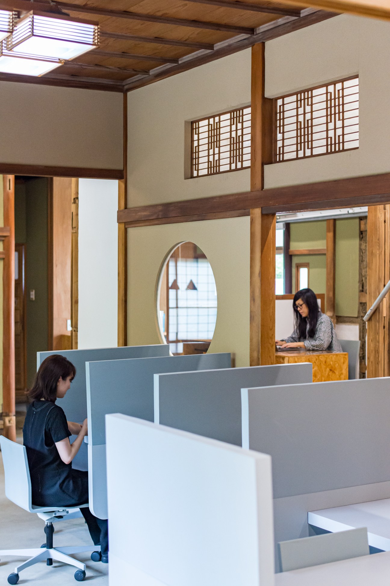 Two women working at desks separated by modular panels in a light-filled converted residence.