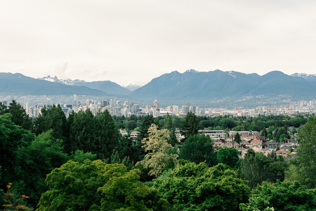 Vancouver cityscape with downtown skyline, forested residential areas, and snow-capped mountains in background