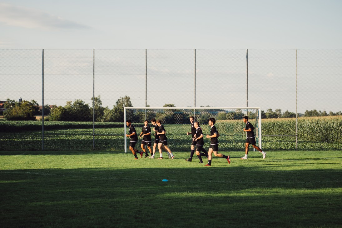 Soccer players in black uniforms running together during training on a grass field with goal posts visible