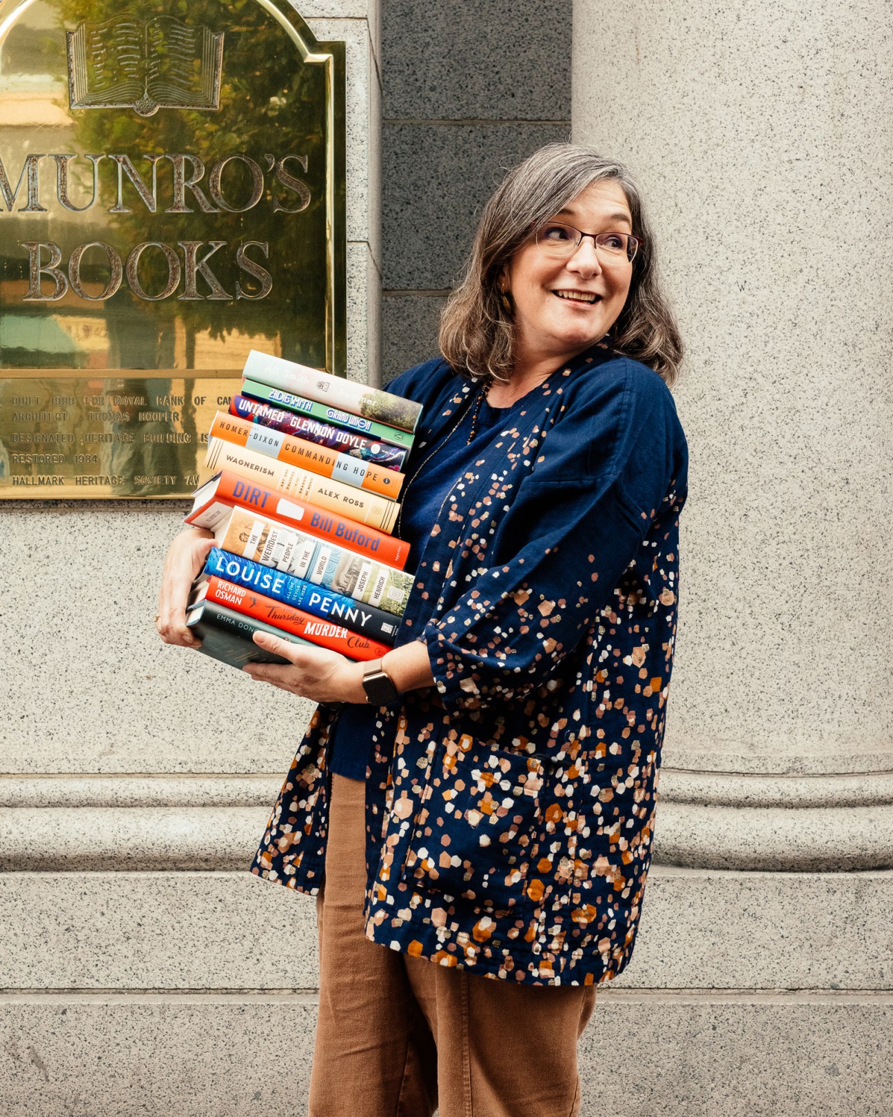 Woman holding stack of books outside Munro's Books storefront in Victoria.