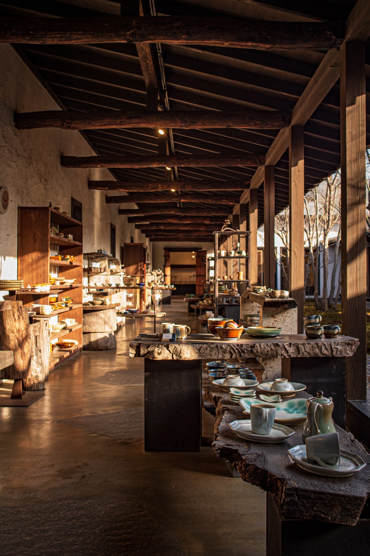 Interior of Casa Mutina showroom with wooden shelving, tableware displays, and exposed wooden beam ceiling.