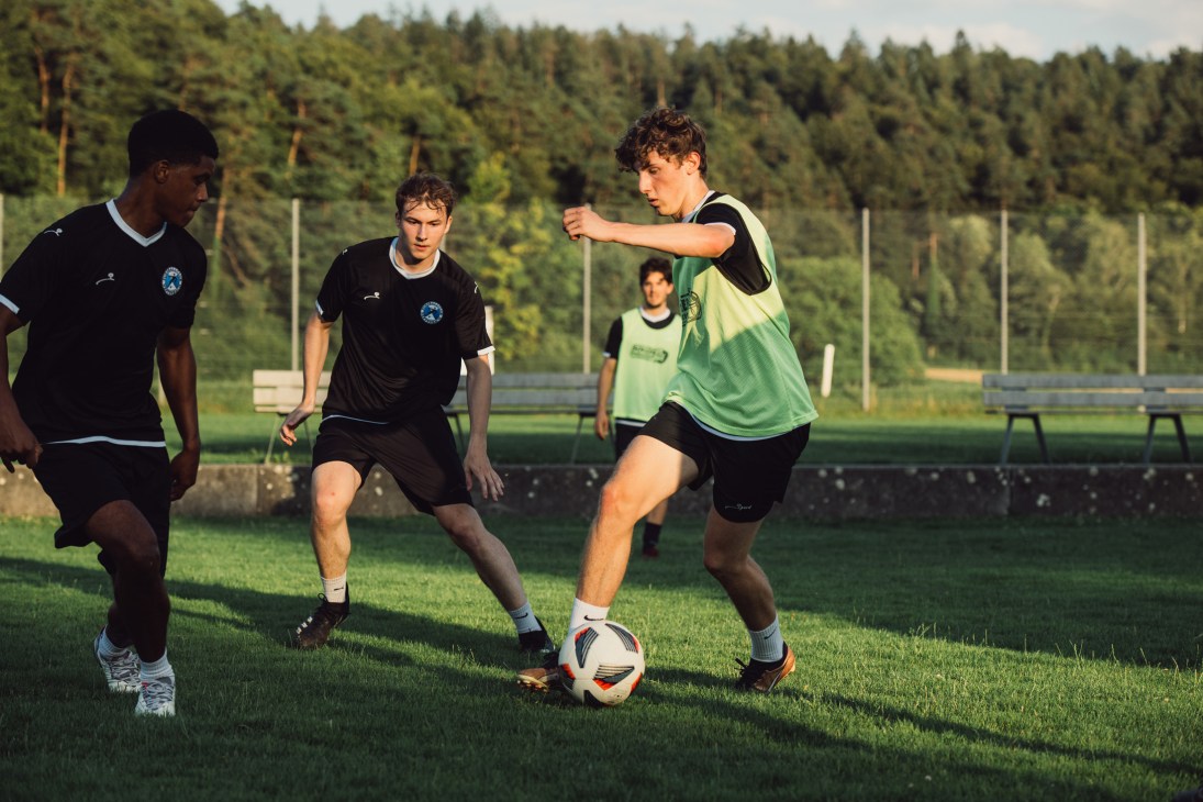 Soccer players in black and green jerseys competing for the ball during practice on a grass field