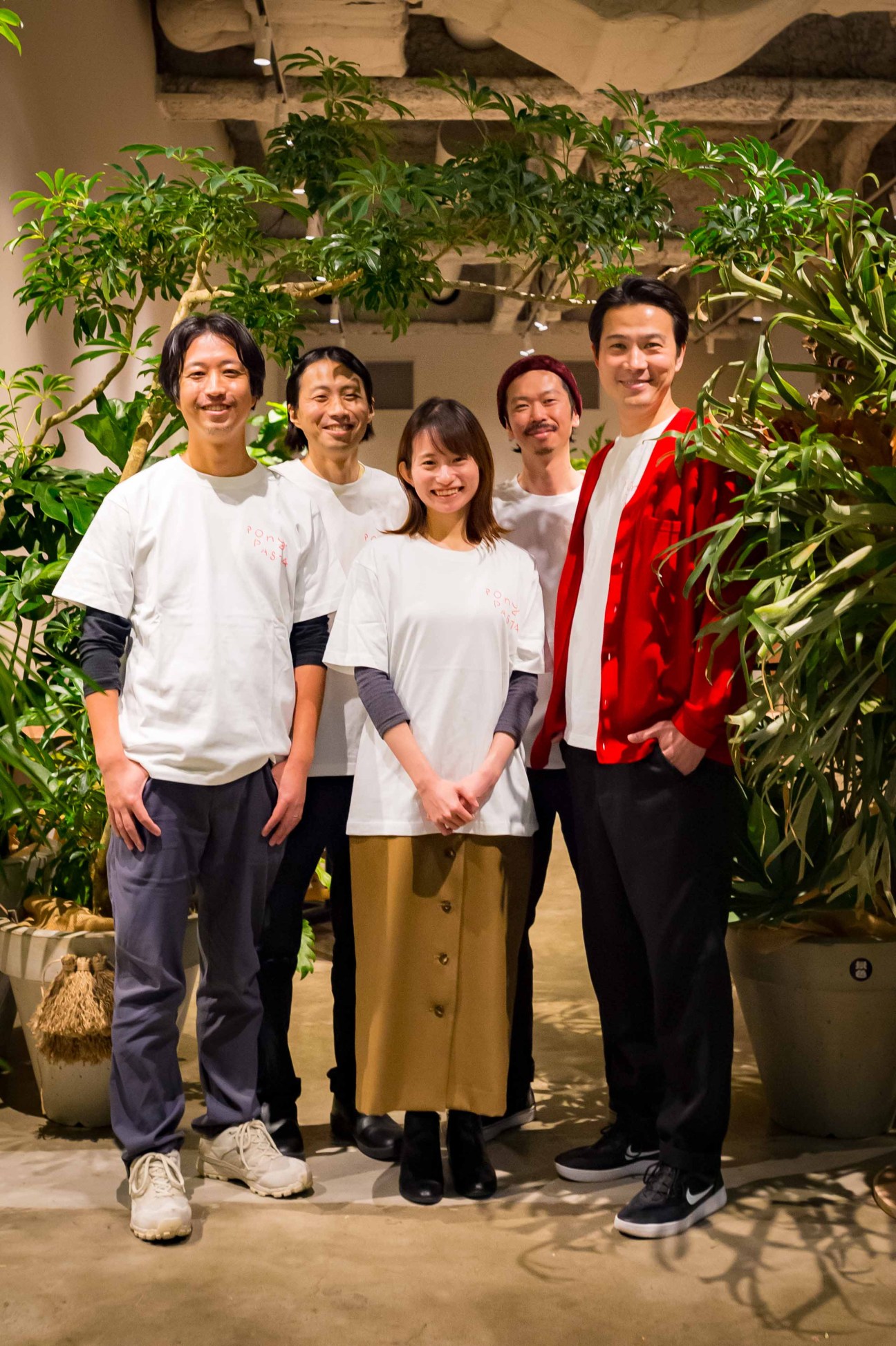 Team of five people posing together indoors surrounded by plants