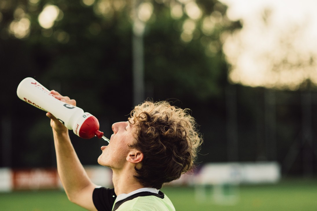Young athlete with curly hair drinking from a sports water bottle outdoors after exercise