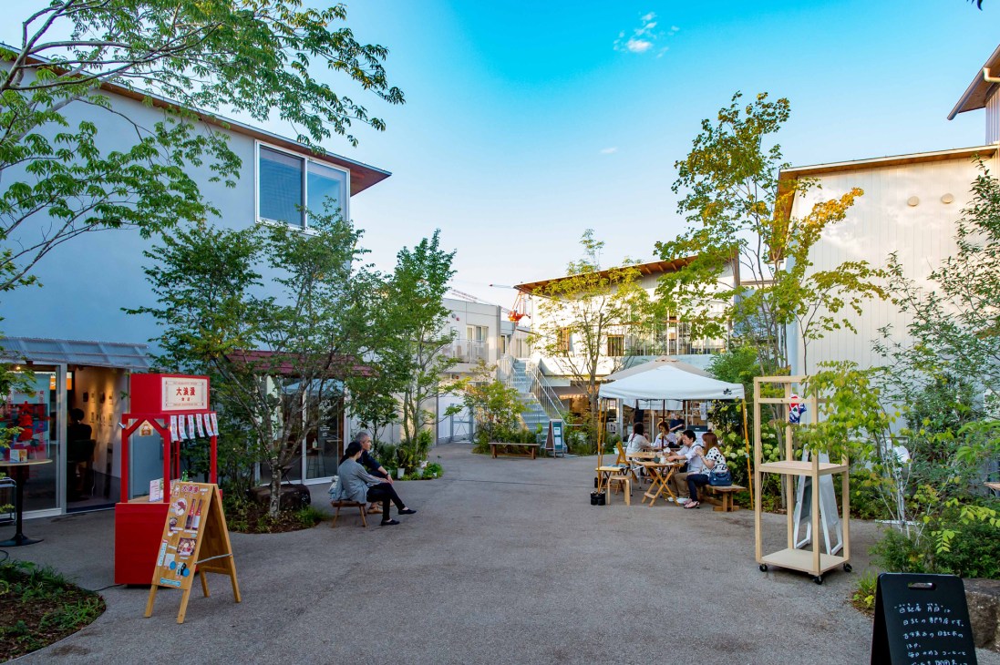 An outdoor courtyard area with modern white buildings, shops, and diners under a clear blue sky.