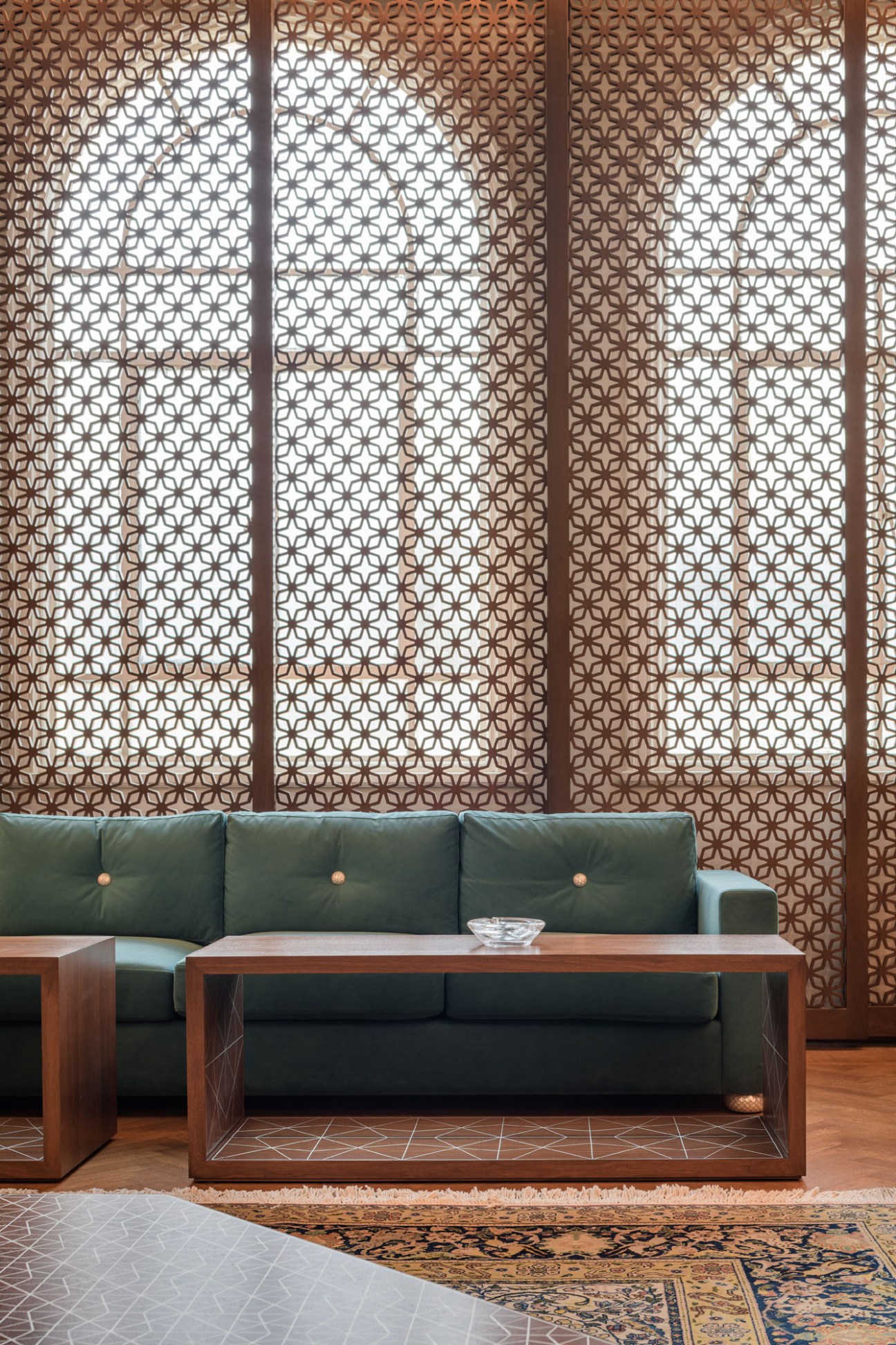Modern lounge area with geometric patterned wood screens, green leather sofa and walnut coffee table