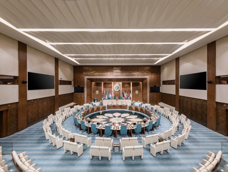 Circular conference hall with concentric white chairs around central table, walnut paneling, and Arabic calligraphy