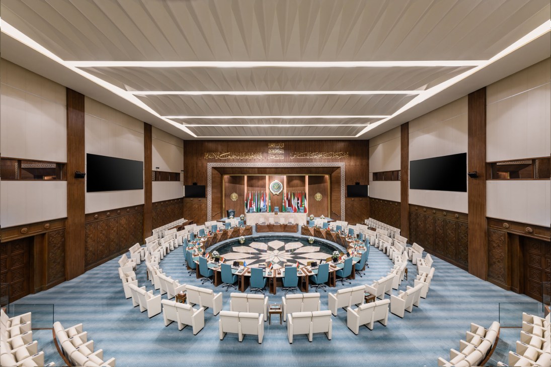 Circular conference hall with concentric white chairs around central table, walnut paneling, and Arabic calligraphy