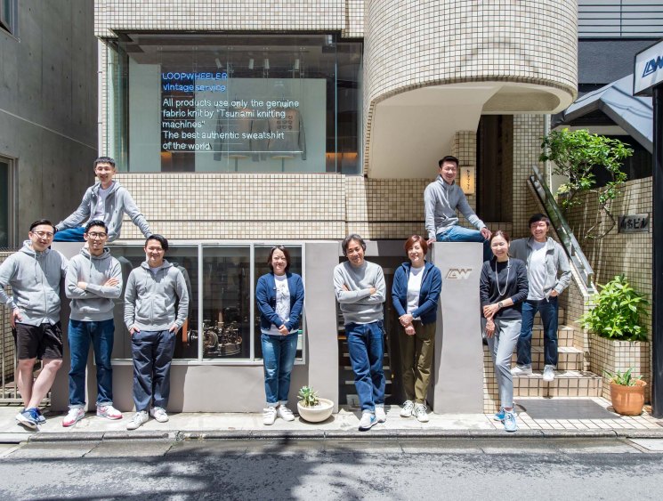 Team of Loopwheeler staff posed outside their Tokyo storefront with signage about their Tsunami knitting machines.