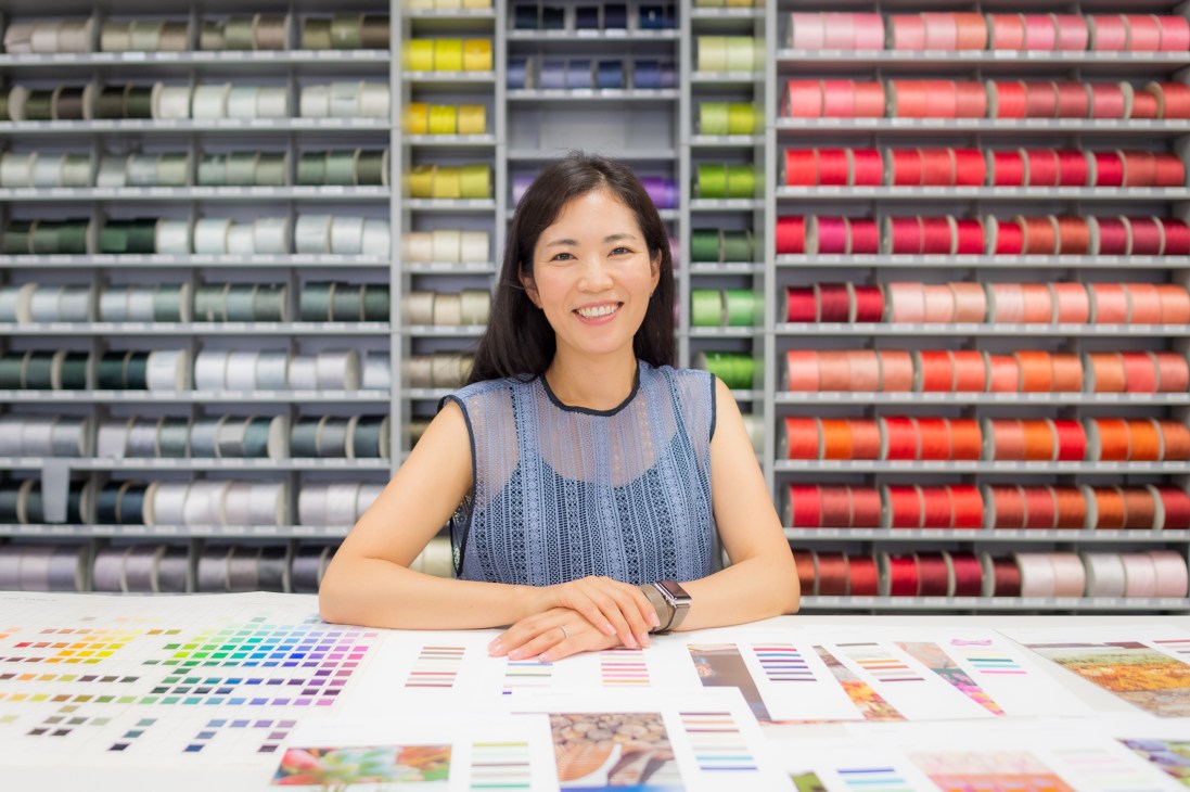 Tamaki Ogiso sits at her desk at the Japan Fashion Colour Association office surrounded by shelves of colorful thread spools